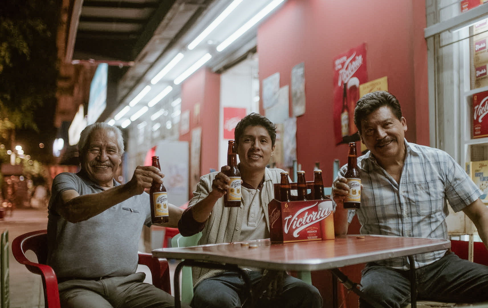 Three men smiling and holding Victoria beers.